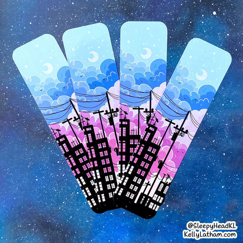 Three tall, narrow decorative panels or flags with a stylized illustration of blue clouds, crescent moons, birds, and black silhouettes of buildings and power lines, set against a starry blue space background. A small watermark at the bottom right reads @SleepyHeadK1 and KellyLatham.