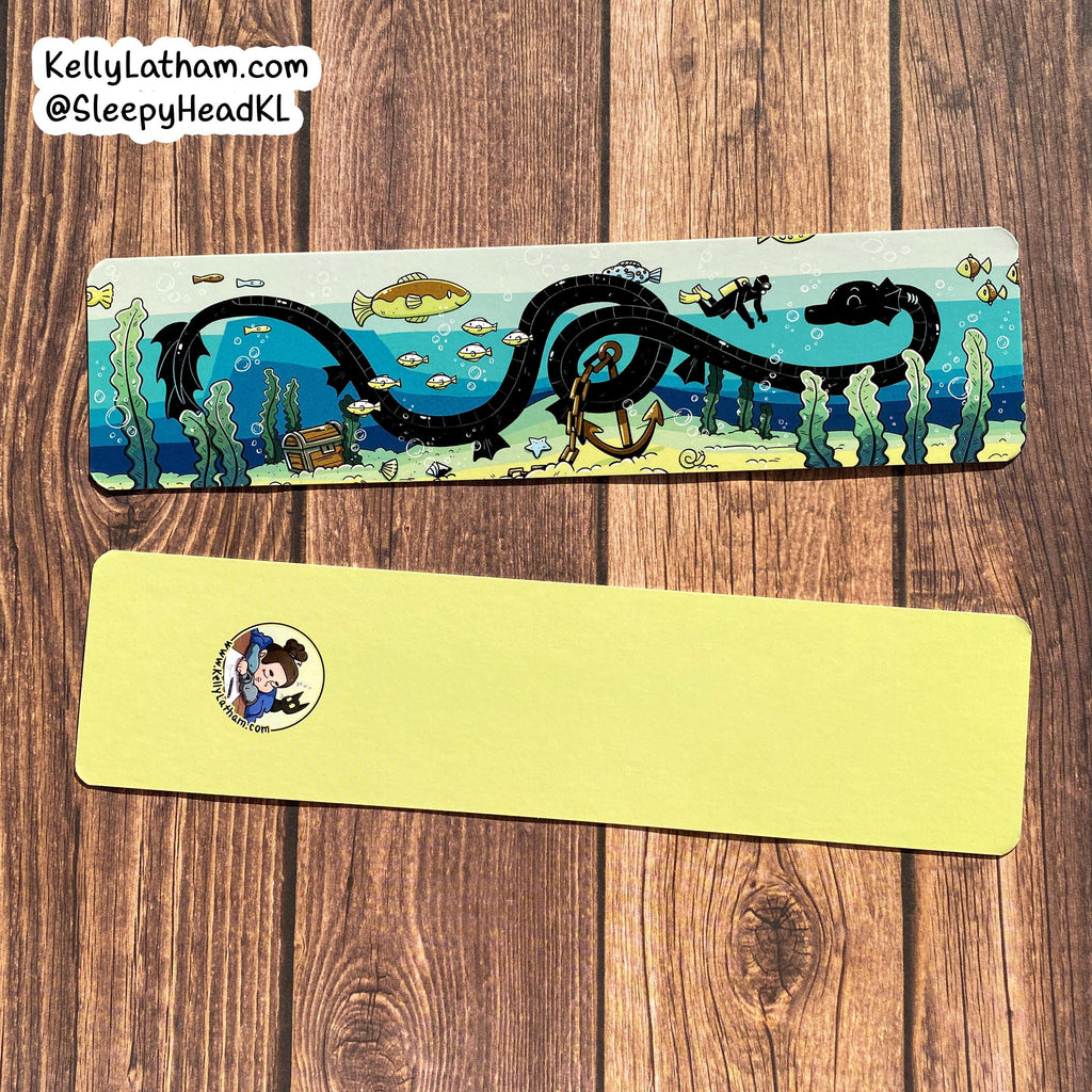 Two rectangular printed cards or bookmarks laid flat on a wooden surface. The top card shows an illustrated underwater scene with a black serpent-like creature, blue water, fish, and small marine details.