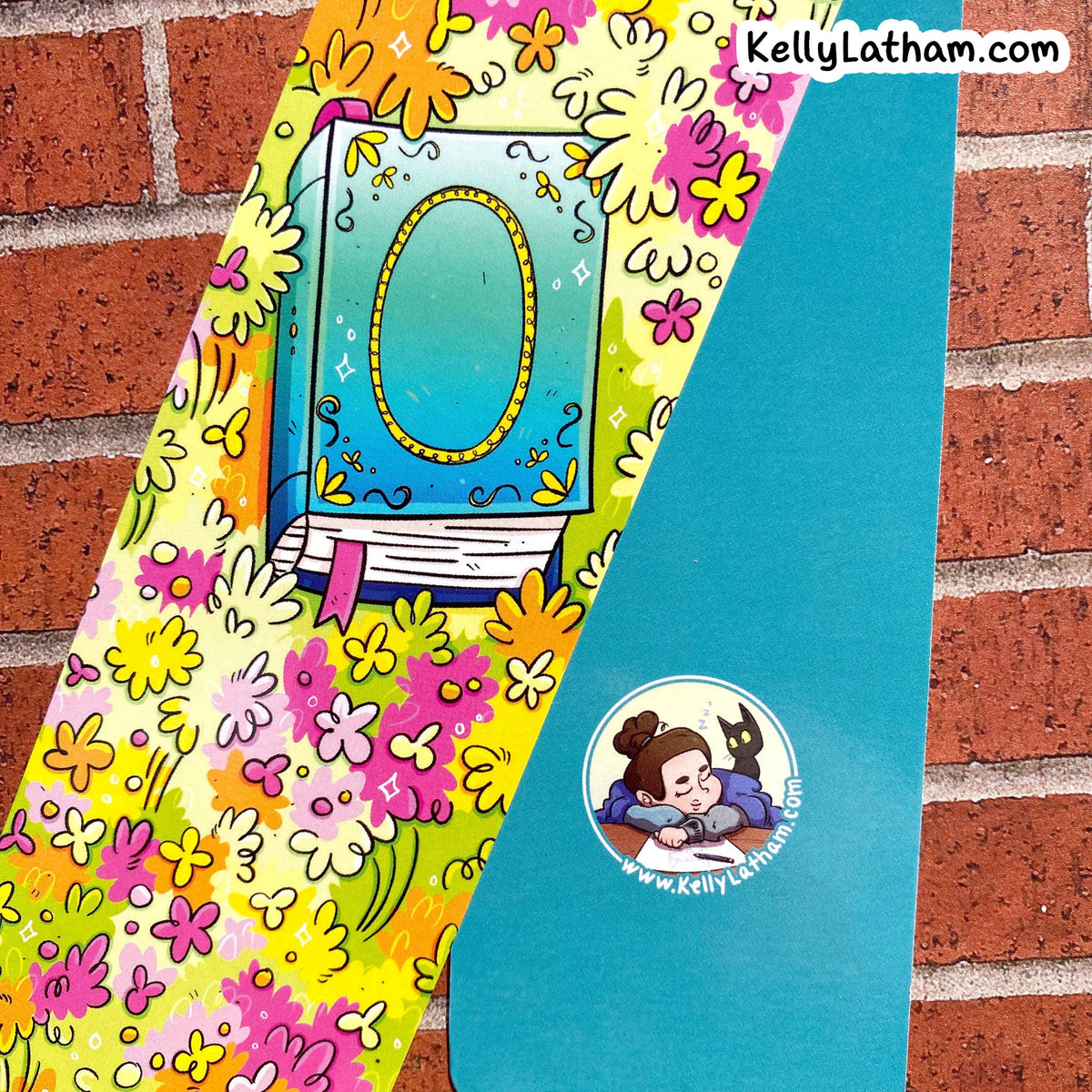 A decorative book-themed sticker or decal sheet shown against a red brick wall background. The sheet features a large illustrated book with an oval mirror on a yellow and pink floral patterned background, alongside a solid teal section with a cartoon character sticker and the text KellyLatham.