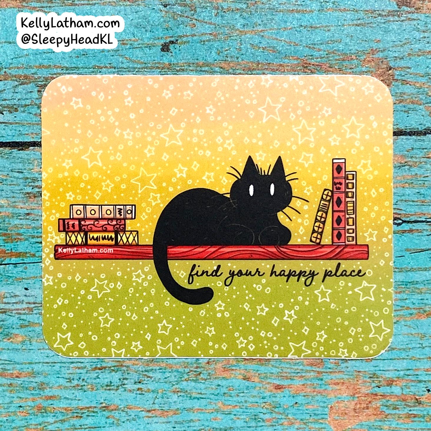 A square printed card or art piece with rounded corners, featuring a black cat sitting on a red shelf against a yellow-to-green gradient background with white stars. The card includes the phrase 'find your happy place' and is photographed on a distressed turquoise wooden surface.