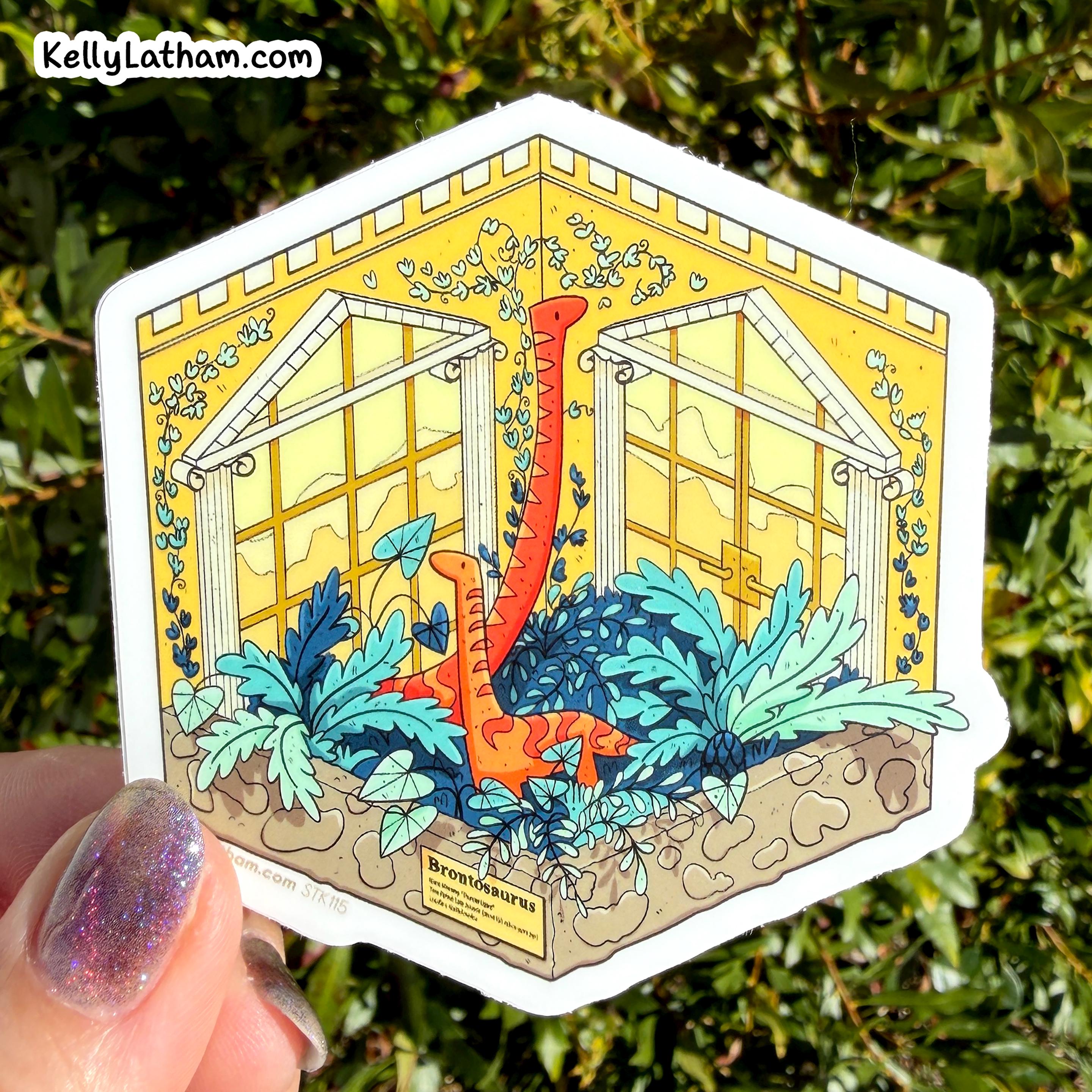 A die-cut sticker featuring a whimsical greenhouse illustration with orange dinosaur-like creatures among blue plants, held by a hand against a background of green foliage. The sticker has a white border and a small label at the bottom reading 'Beware the Dinosaur'.