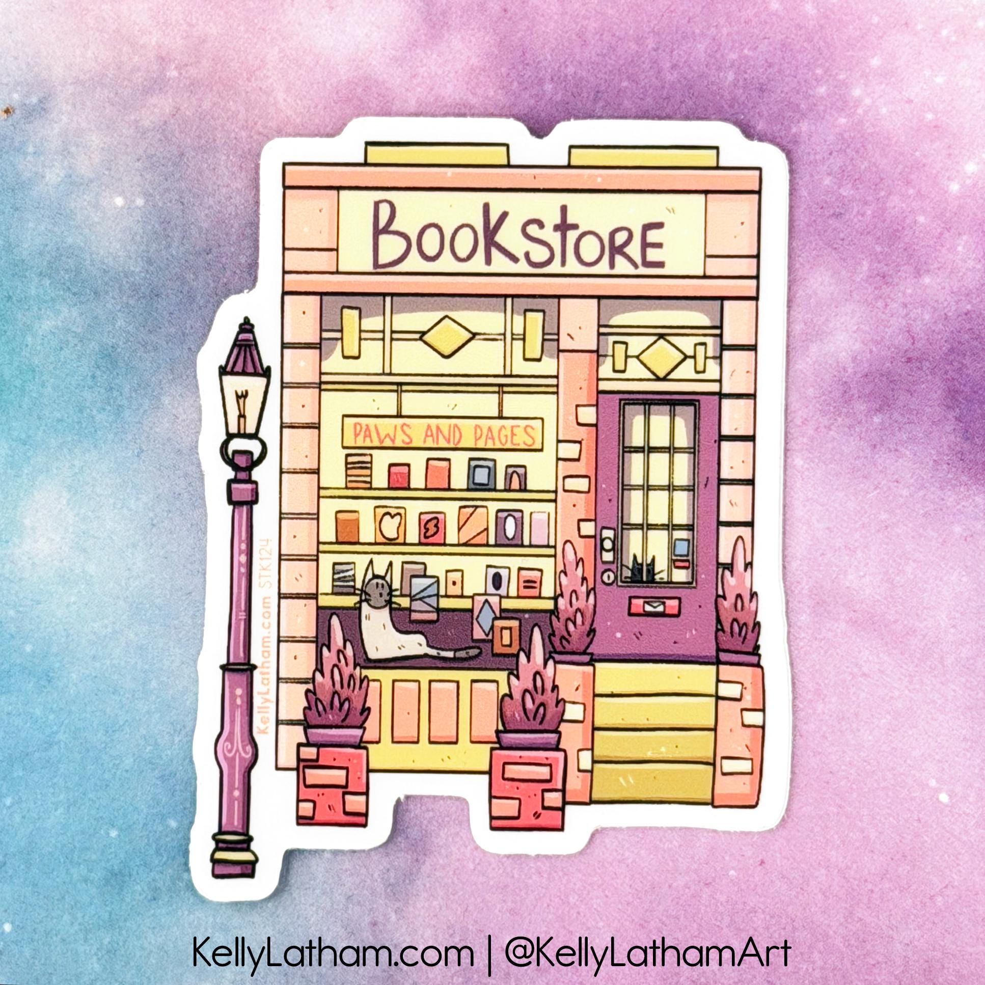 A die-cut sticker featuring a whimsical hand-drawn illustration of a bookstore storefront with a cat sitting inside, set against a pastel watercolor background. The sticker is shown with the text 'KellyLatham.
