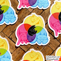 A set of colorful die-cut stickers featuring cartoon cats inside overlapping pastel circles, arranged on a wooden surface. One central sticker shows a black cat on a yellow crescent moon with pink, purple, green, and blue circles behind it.