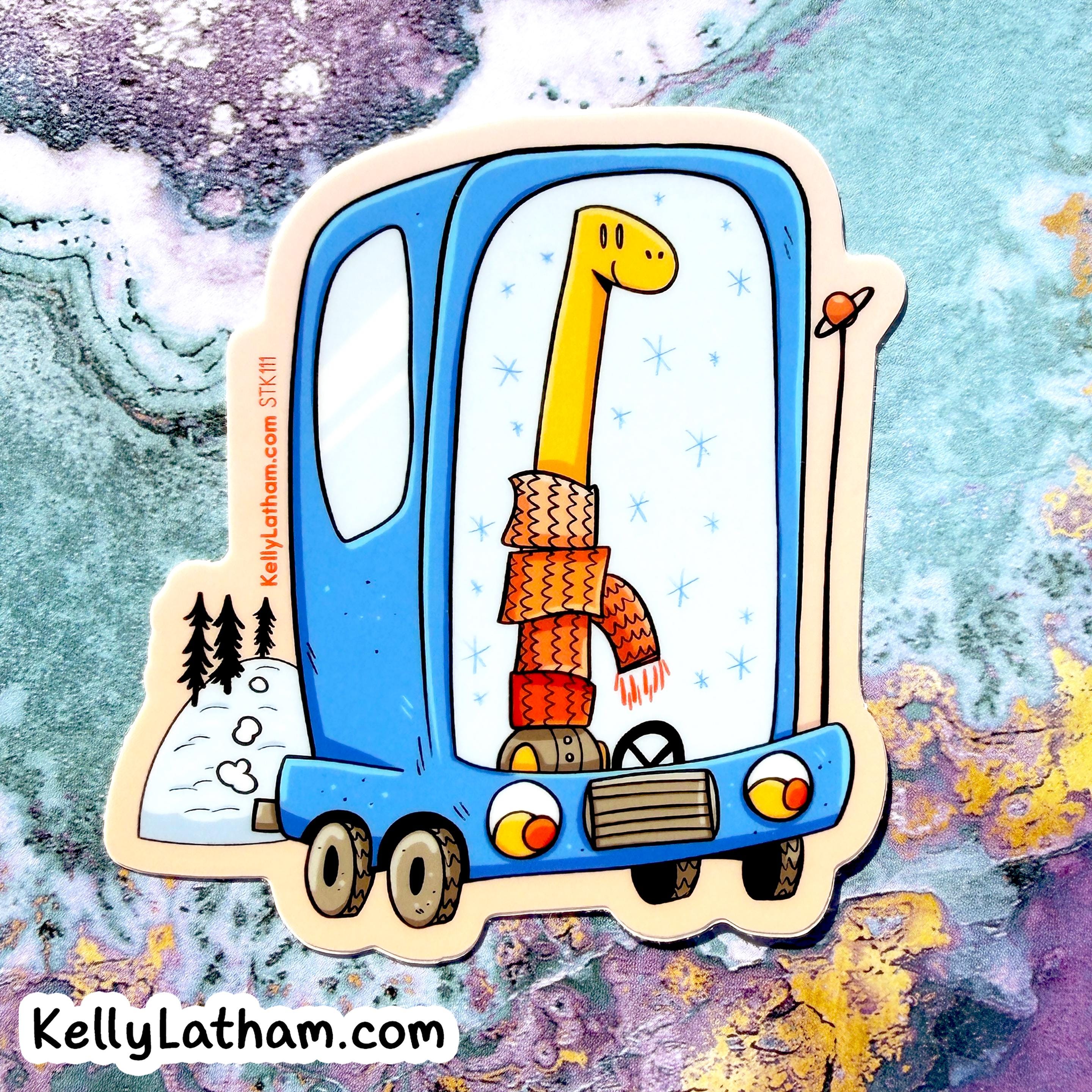 A die-cut sticker featuring a whimsical illustration of a long yellow giraffe wearing an orange knit sweater and scarf inside a blue vehicle, shown on a marbled pastel background. The sticker includes the text 'KellyLatham.