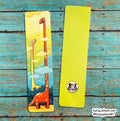 Two slim bookmarks laid flat on a distressed turquoise wood surface. One bookmark is blank bright yellow-green, and the other has a colorful illustration of two long-neck dinosaurs in a sky with clouds.