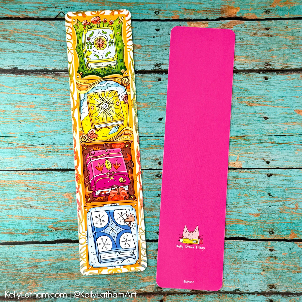 Two bookmarks from Kelly Oshea's 'Oh, Dear Things' card deck are displayed on a rustic, weathered teal wooden background. The left bookmark is decorated with colorful illustrations of tarot cards (The Fool, The Sun, The Devil, The World) in a yellow, orange, and blue palette.