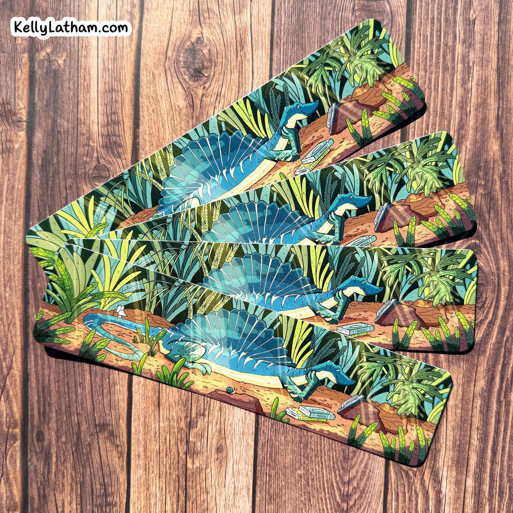 Set of three bookmarks with a tropical design featuring dinosaurs and foliage on a wooden surface.