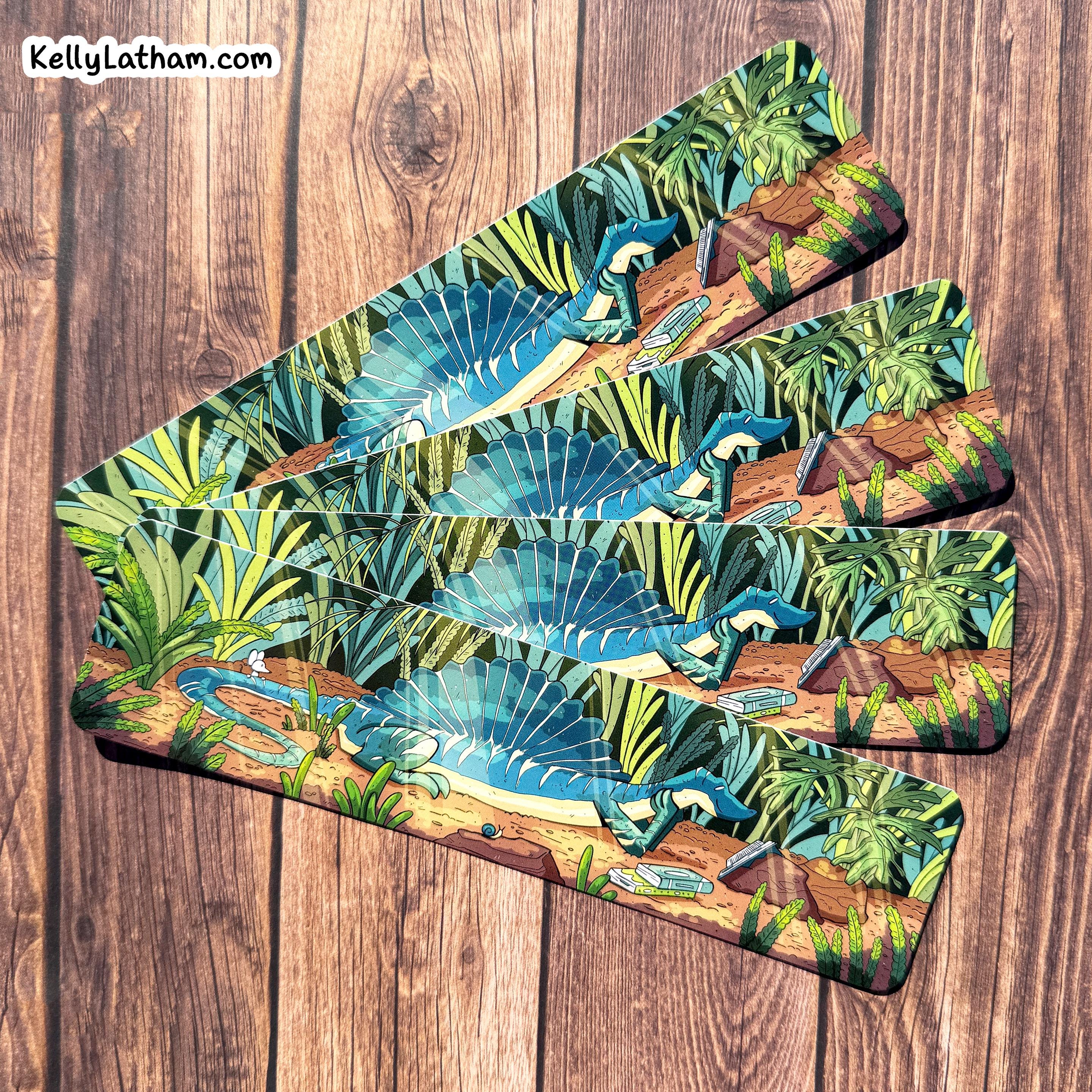 Set of three bookmarks with a tropical design featuring dinosaurs and foliage on a wooden surface.