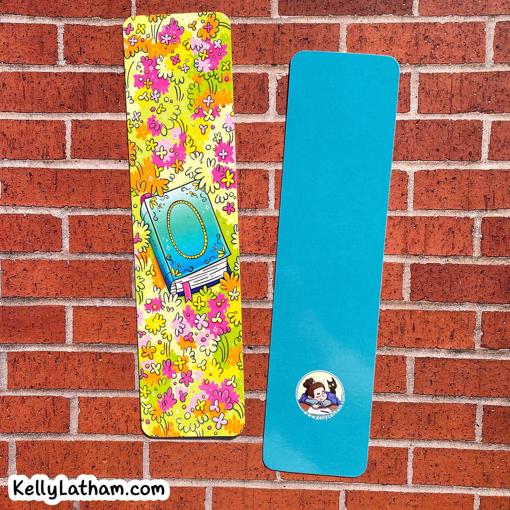 Two yoga mats displayed against a red brick wall background. The left mat features a vibrant yellow, pink, and orange floral pattern with a central illustration of a blue book.