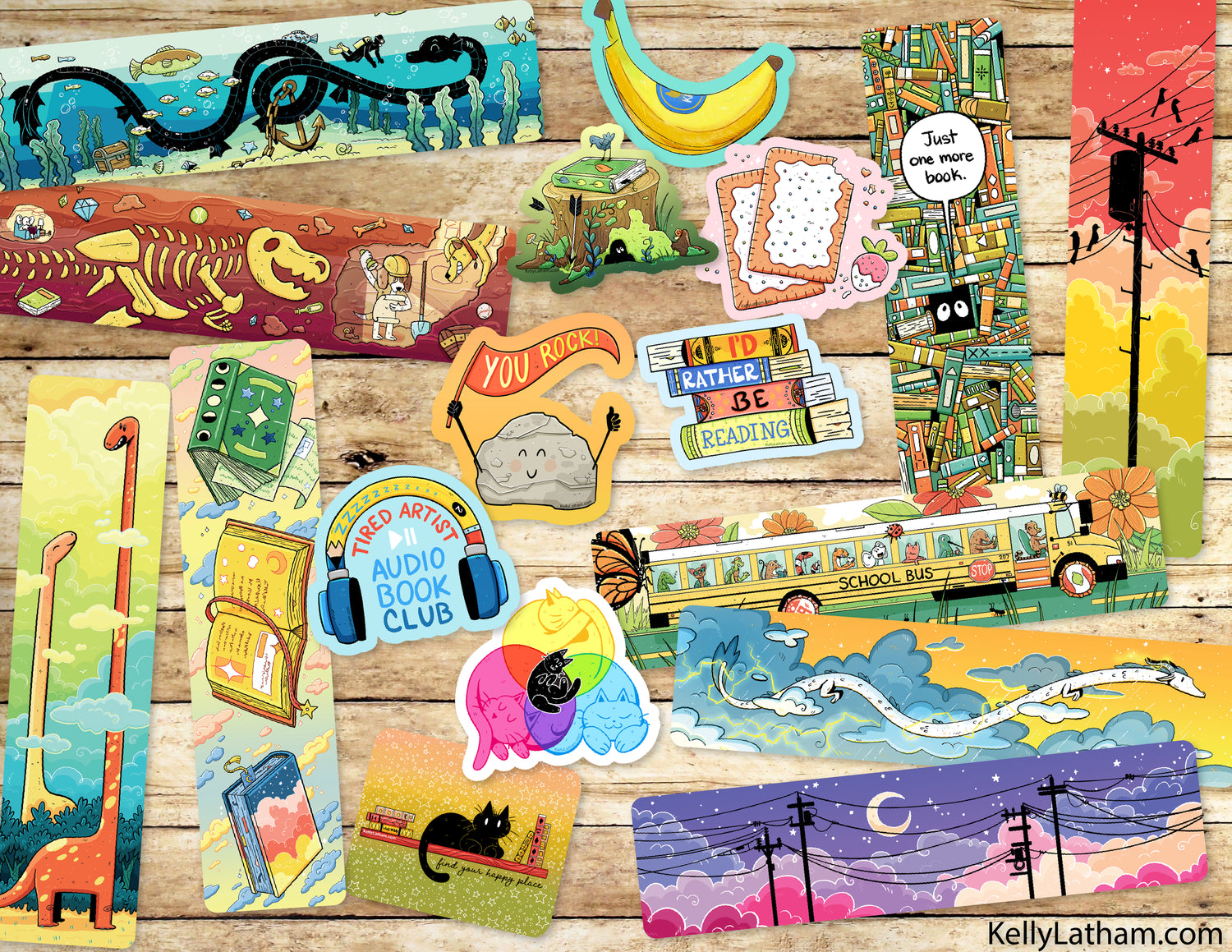 A flat lay of colorful illustrated bookmarks or bookmark strips arranged on a rustic wood surface. The designs include a dinosaur skeleton, bananas, books, a school bus, a cat, a butterfly, a rainbow, and whimsical text like 'You are enough!' and 'Readers at Reading!'.