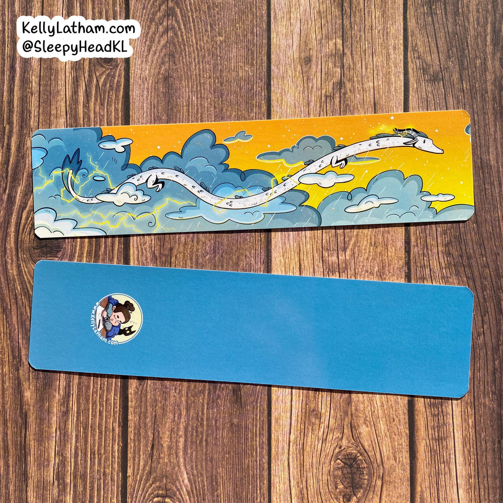 Two bookmarks on a wooden surface, one with a dragon design and the other blue with a sticker.