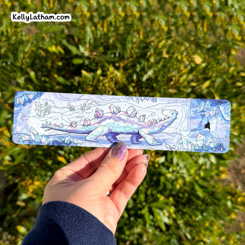 Hand holding a rectangular object with a blue and white design against a green leafy background