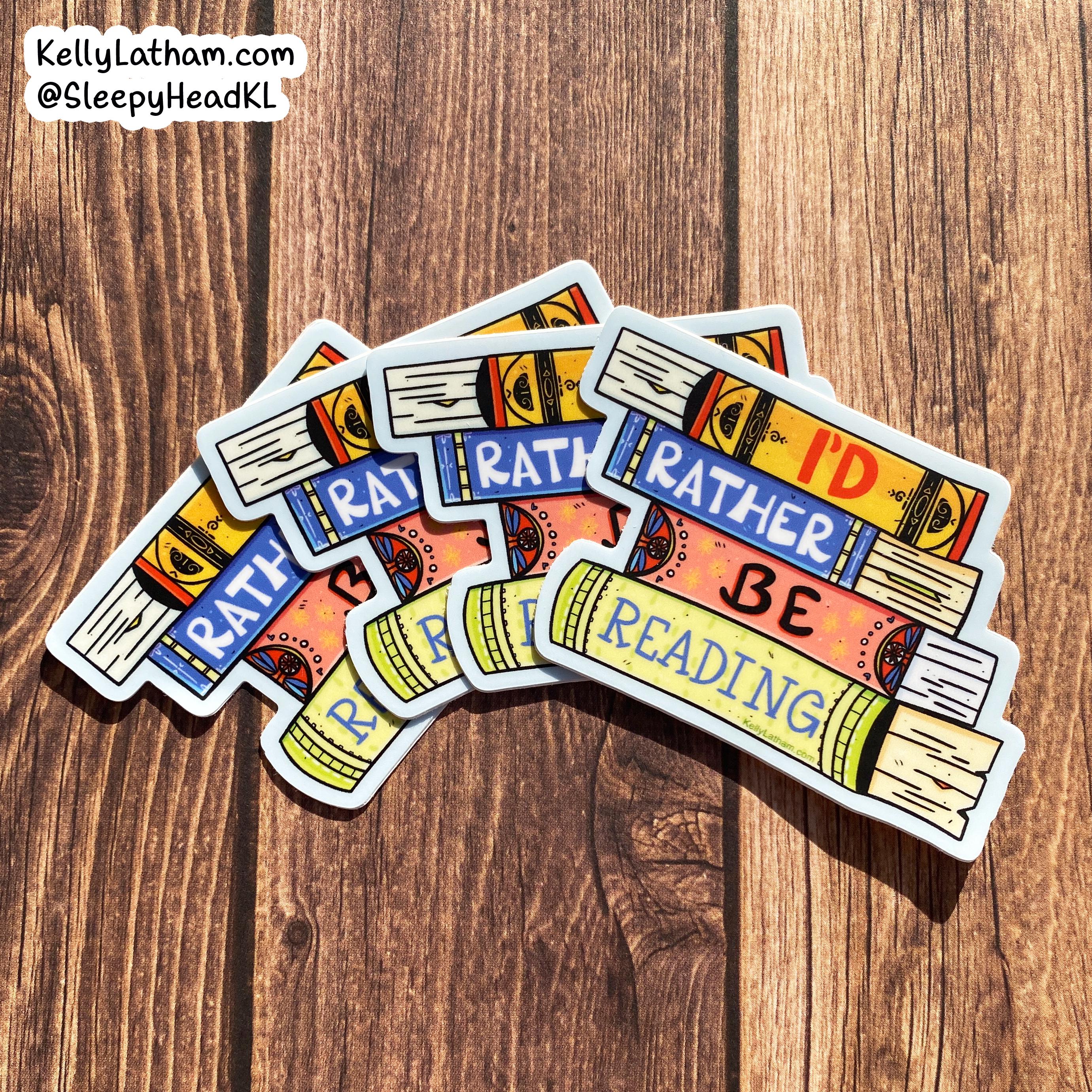 Four die-cut stickers shaped like stacked books with the phrase 'I'D RATHER BE READING' in colorful lettering, arranged on a brown wood surface. A Shopify watermark is visible in the top-left corner.