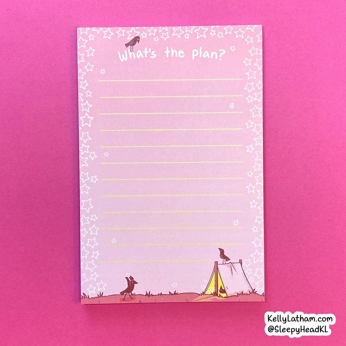 A pink notepad with lined writing space, decorated with white star borders, the handwritten phrase 'What's the plan?' at the top, and small whimsical illustrations of a bird, dog, and tent along the bottom. The pad is photographed on a bright pink background.