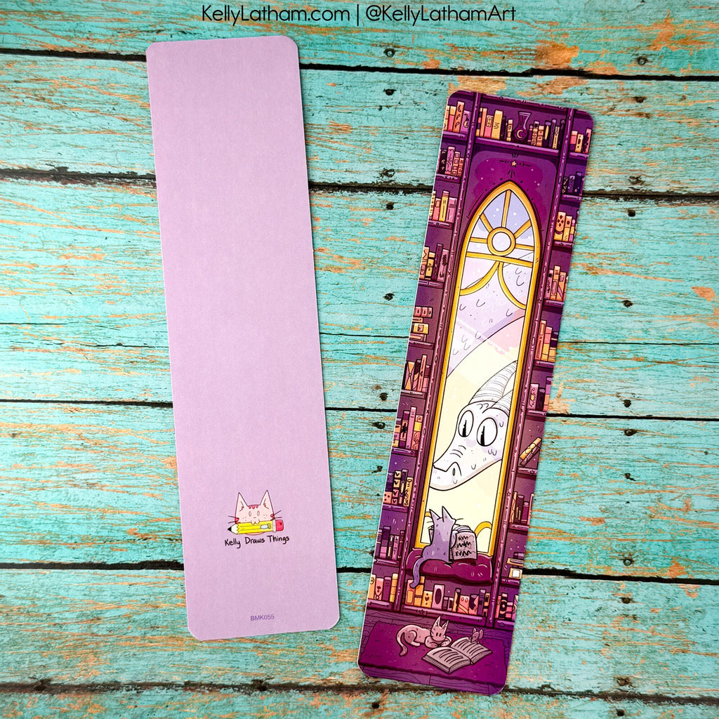 Two bookmarks on a wooden surface, one purple with a cat illustration and the other with a stained glass design.