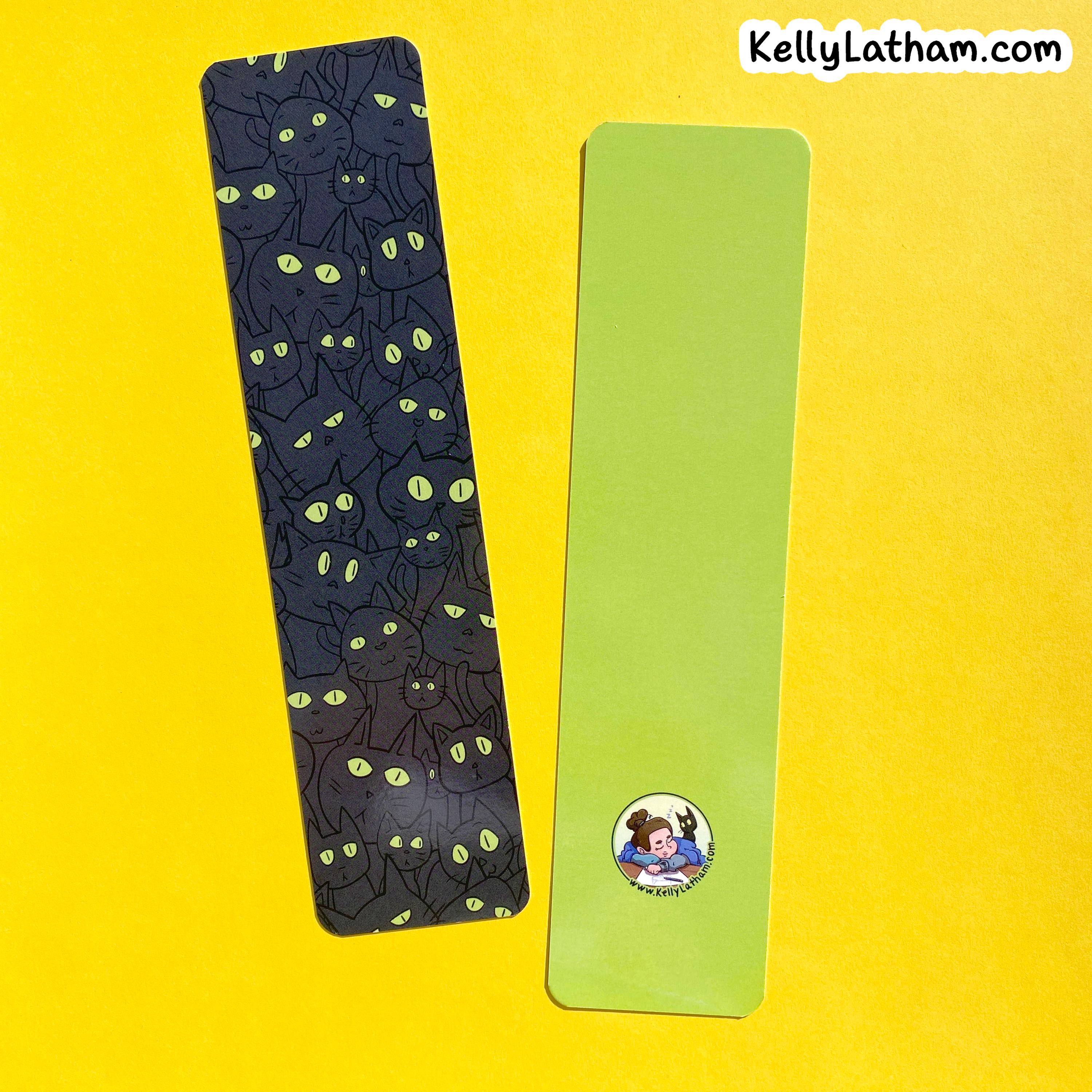 Two bookmarks on a bright yellow background. One bookmark is dark charcoal/black with a repeating pattern of cartoon cats and glowing green eyes.
