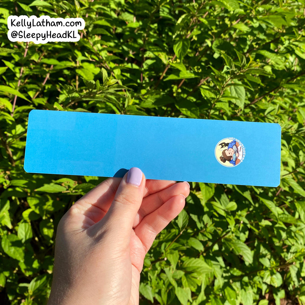 Hand holding a blue strip with a sticker featuring a cartoon character against a green leafy background.