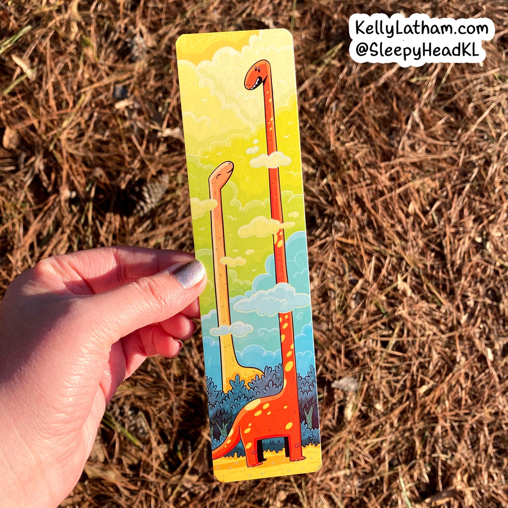 Hand holding a colorful bookmark with a long orange creature design against a natural background.
