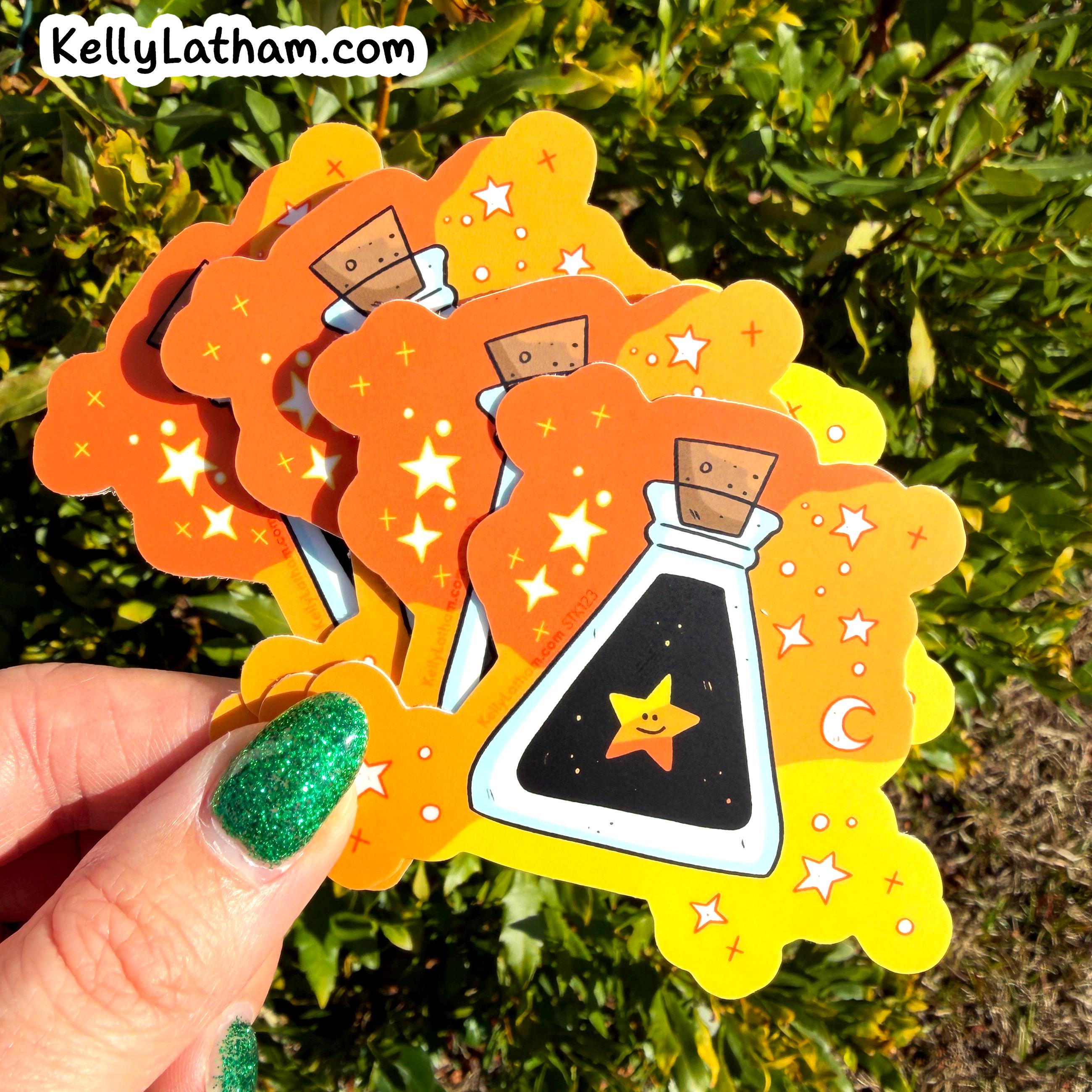 Decorative stickers with a witch design held by a hand against a green leafy background.