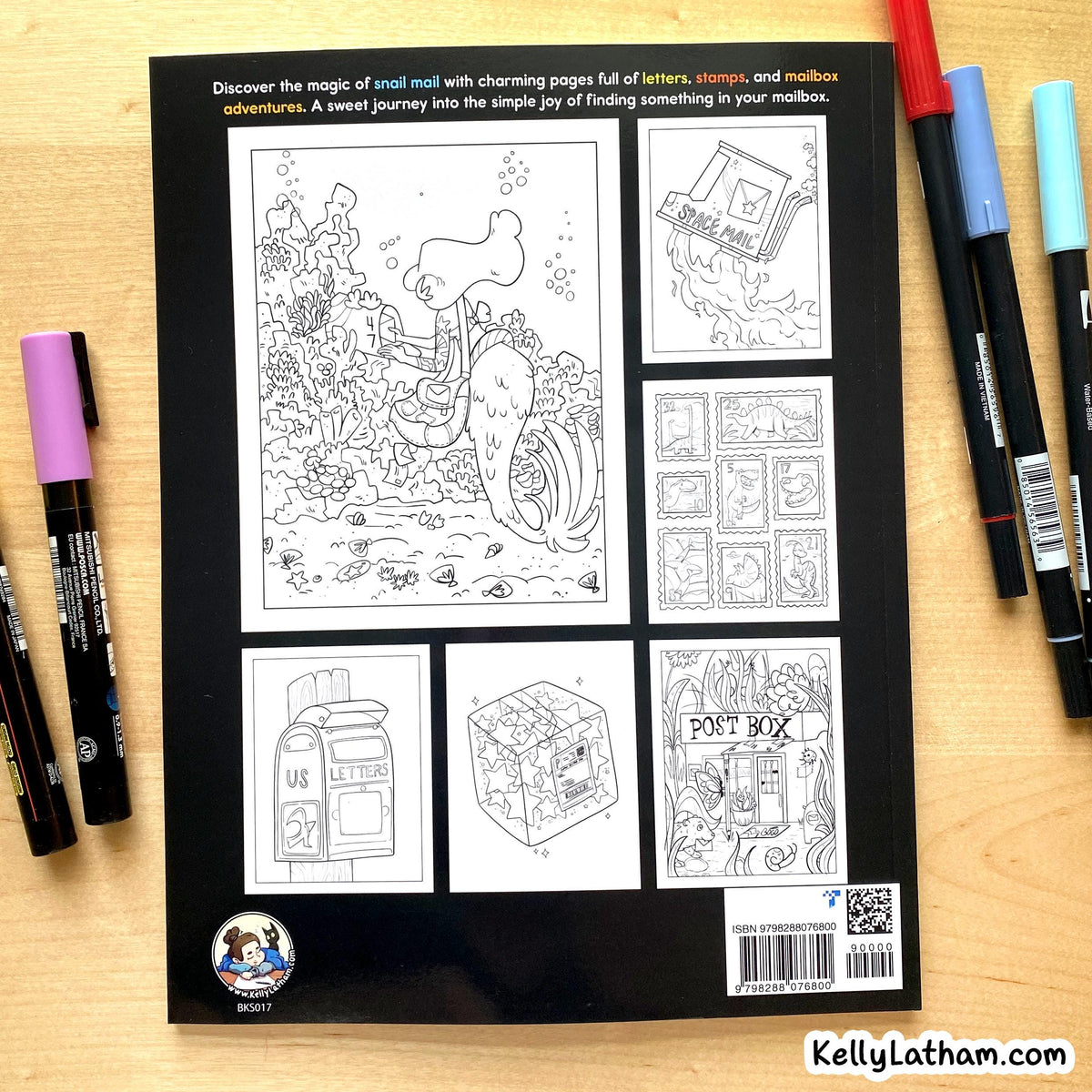 A coloring book for kids with a black cover displaying six black-and-white mail-themed illustration pages, photographed on a light wood surface with colored markers placed around it.