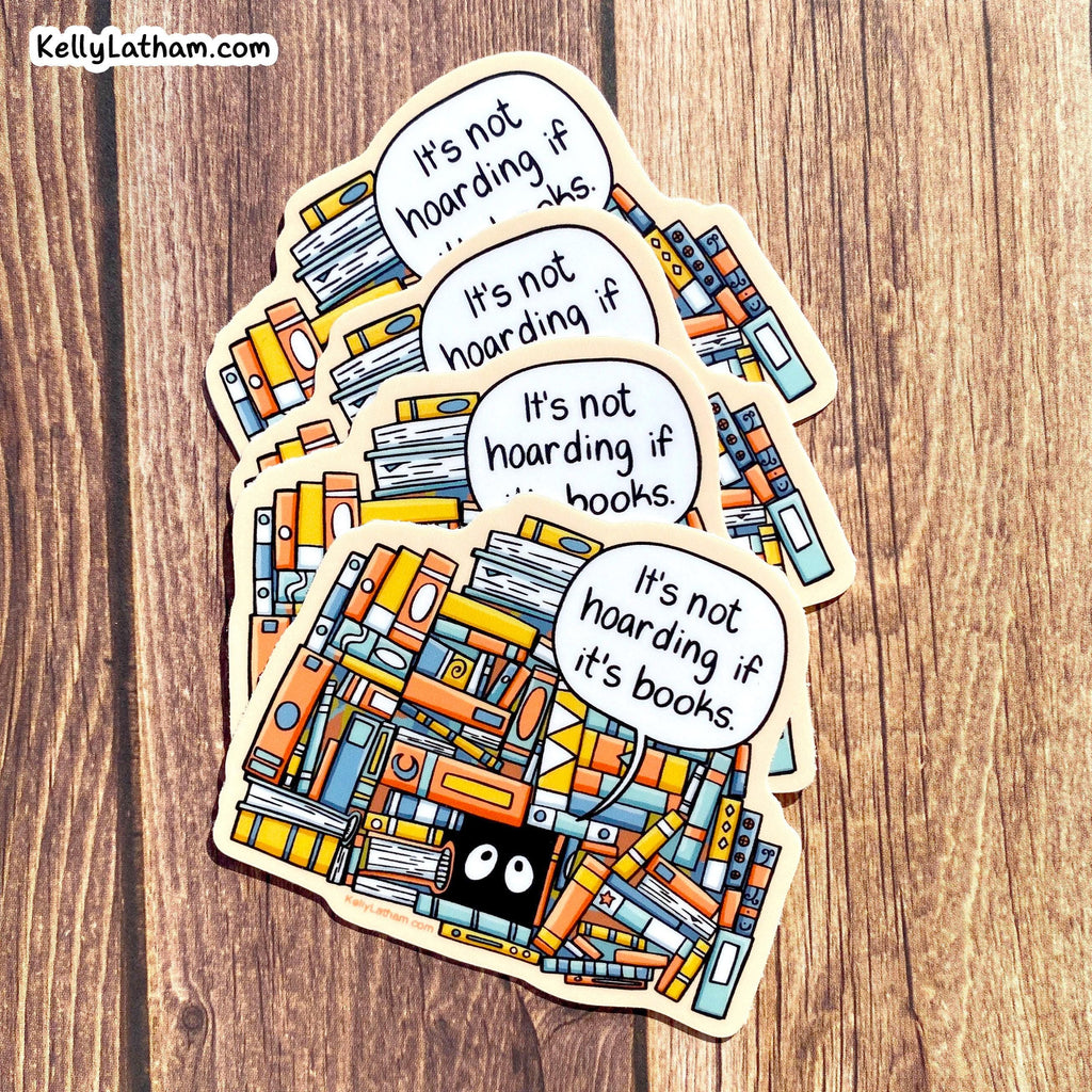 A set of die-cut stickers featuring a colorful illustration of books and three speech bubbles that read 'It's not hoarding if it's books.' The stickers are arranged in a fan shape on a wooden surface.