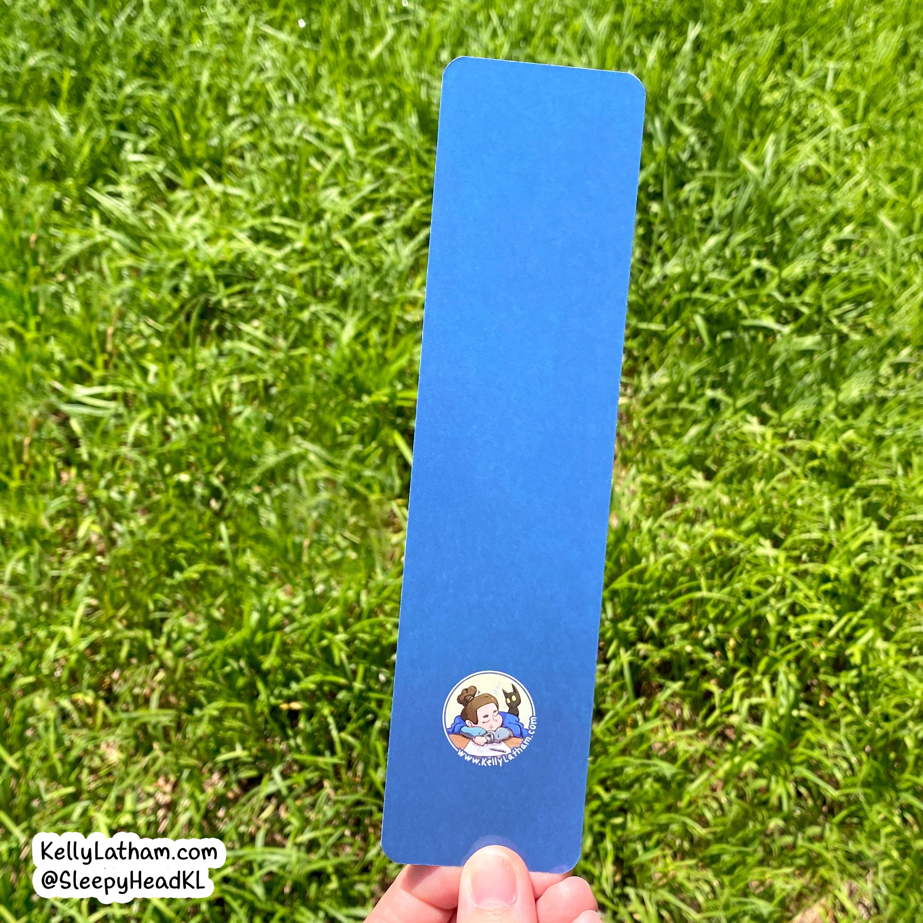 A blue rectangular card or bookmark with a small circular 'The Great Mouse Detective' logo near the bottom, held by a hand against a background of green grass.