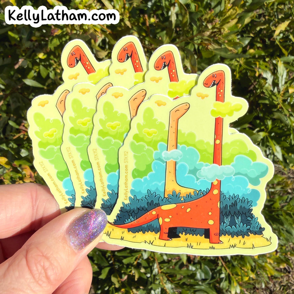 A hand with glittery purple nail polish holds a fan of five die-cut stickers featuring a whimsical orange long-neck dinosaur among green trees and blue clouds, set against a background of green foliage. The text 'KellyLatham.