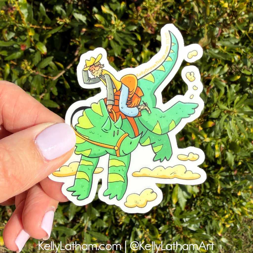 Hand holding a sticker of a person riding a green dinosaur with a person in an orange life jacket against a green leafy background.