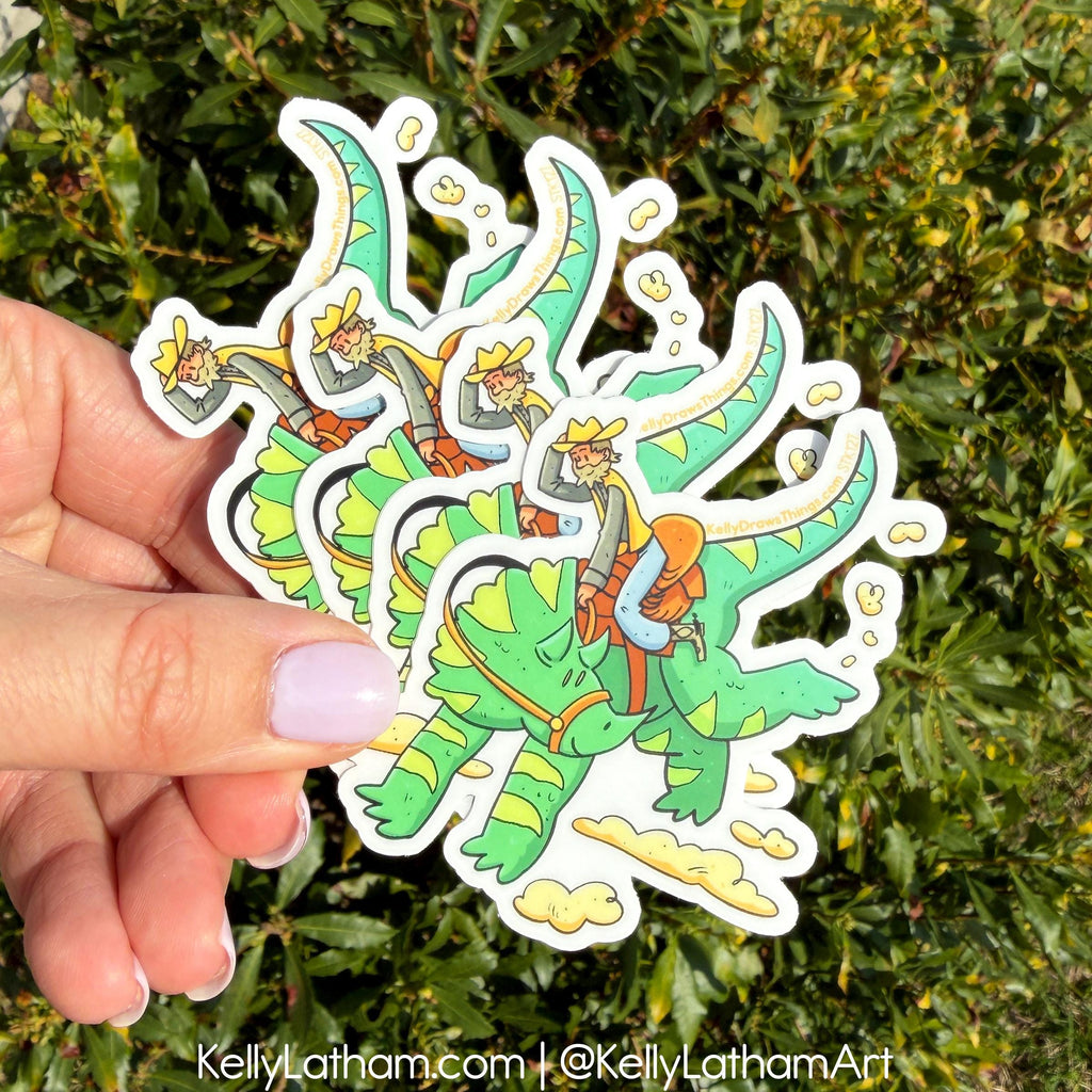 Hand holding a colorful sticker of a character riding a dragon with green and orange design against a green leafy background.