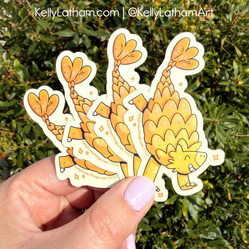 Hand holding a sticker with a cartoon ankylosaurus design against a green leafy background