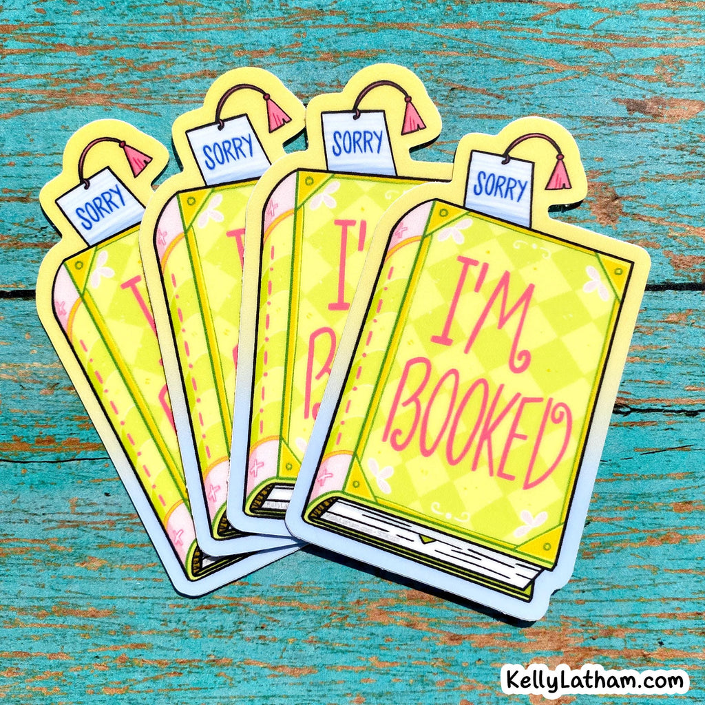Five cartoon book-shaped stickers fanned out on a distressed teal wooden surface. Each sticker says 'SORRY' on a tag at the top and 'I'M BOOKED' on the front in pink lettering.