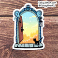 A die-cut sticker featuring an illustration of a black cat standing in front of an ornate blue doorway that opens to a pastel sky with clouds, placed on a wooden surface. The sticker has a white border, and the text 'KellyLatham.