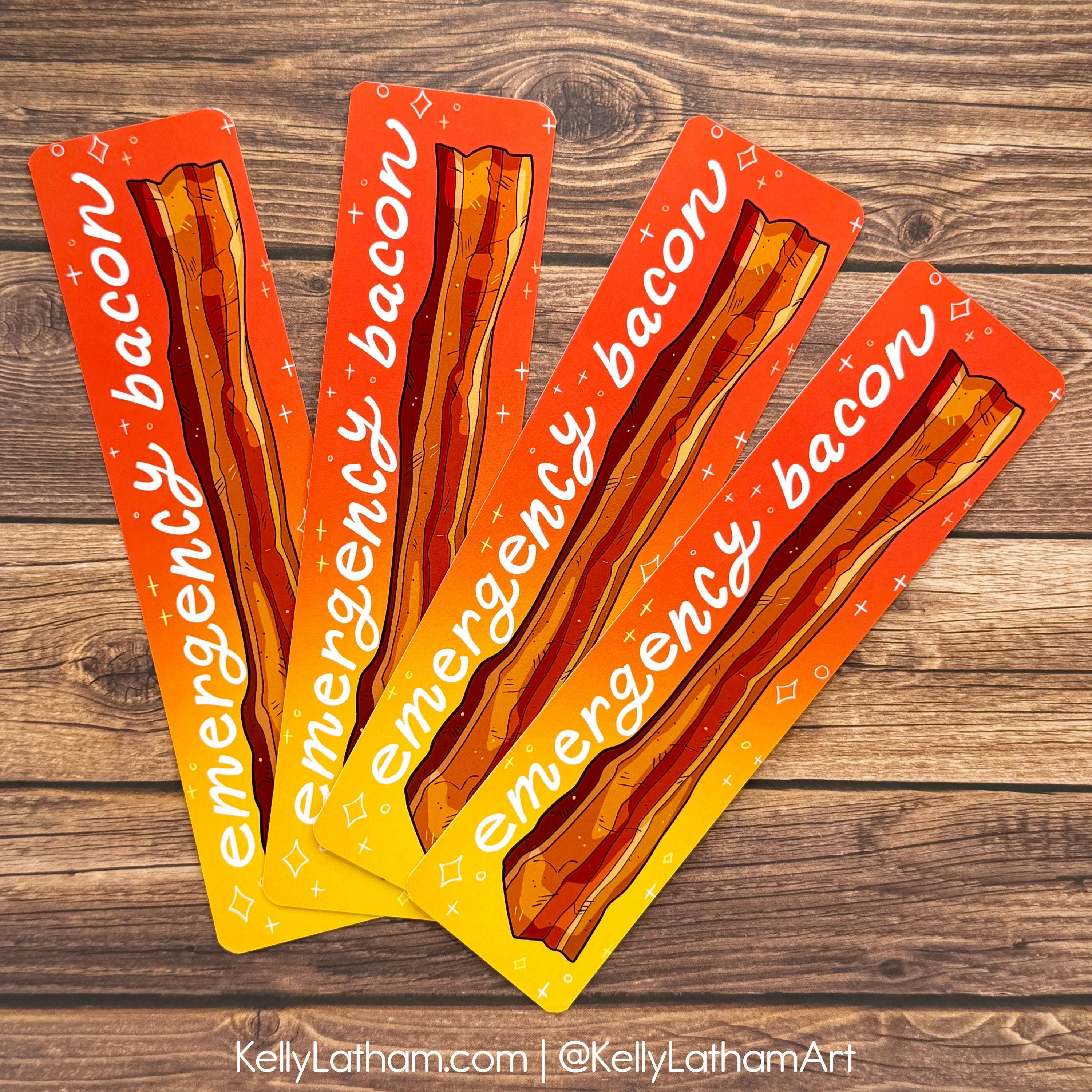 Four bacon-themed bookmarks fanned out on a dark wood background. Each bookmark features an illustration of crispy bacon strips on a red-to-yellow gradient background with the words 'emergency bacon' written in white script.
