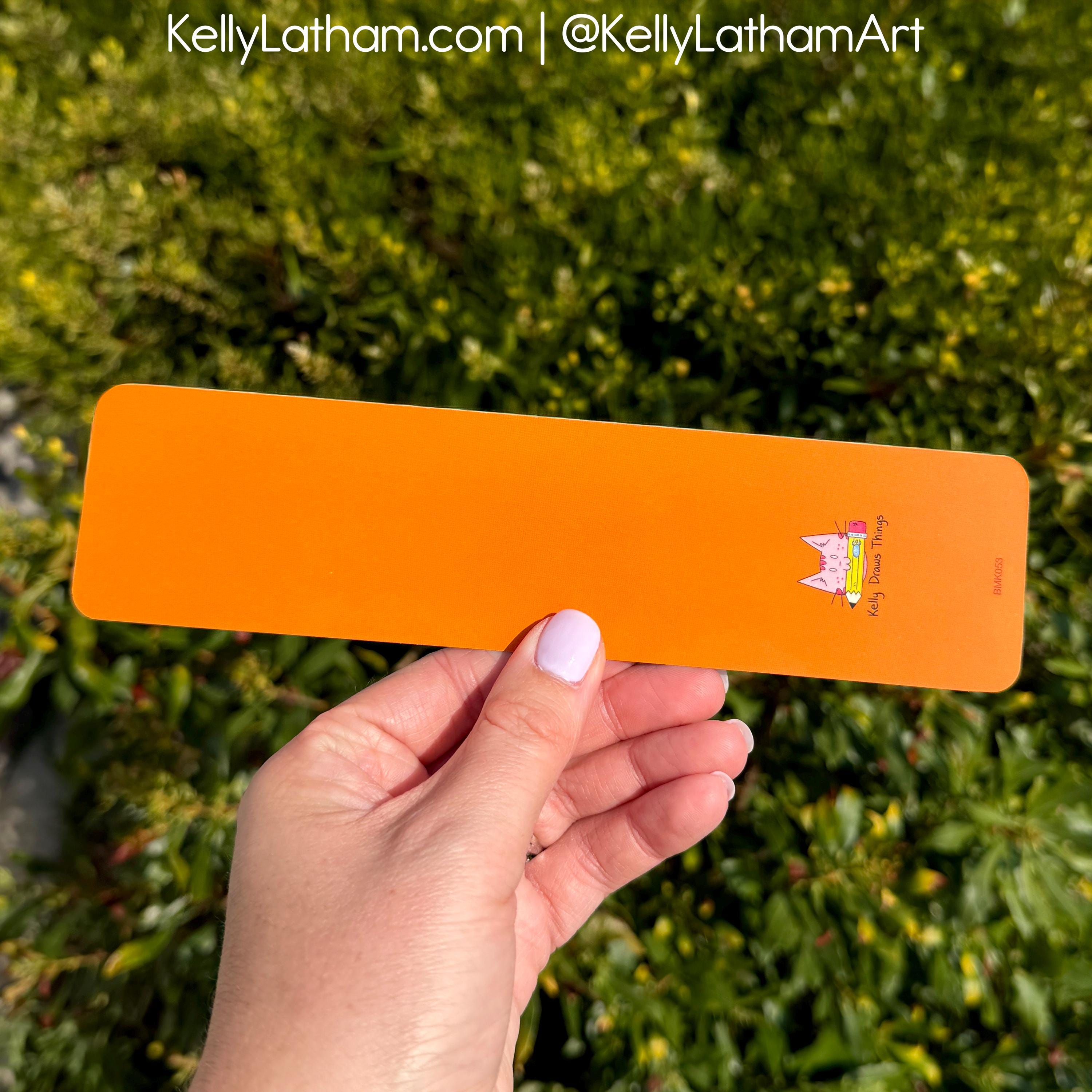 Hand holding an orange slip with a cat design against a green leafy background