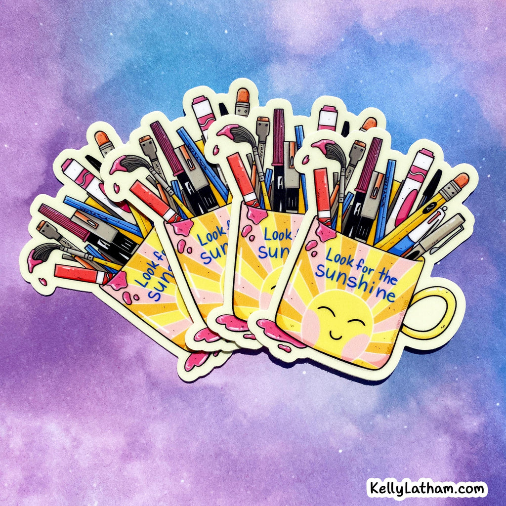 Three die-cut stickers featuring yellow smiley-face mugs filled with colorful paintbrushes and art tools, arranged in a fan shape against a purple and blue watercolor background. The stickers have the text 'Look for the Sunshine' and are shown with a small 'KellyLatham.
