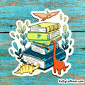 A die-cut sticker featuring a stack of colorful books with cartoon dinosaurs and plants, shown on a distressed blue wooden background. The sticker has a white border and the text 'KellyLatham.