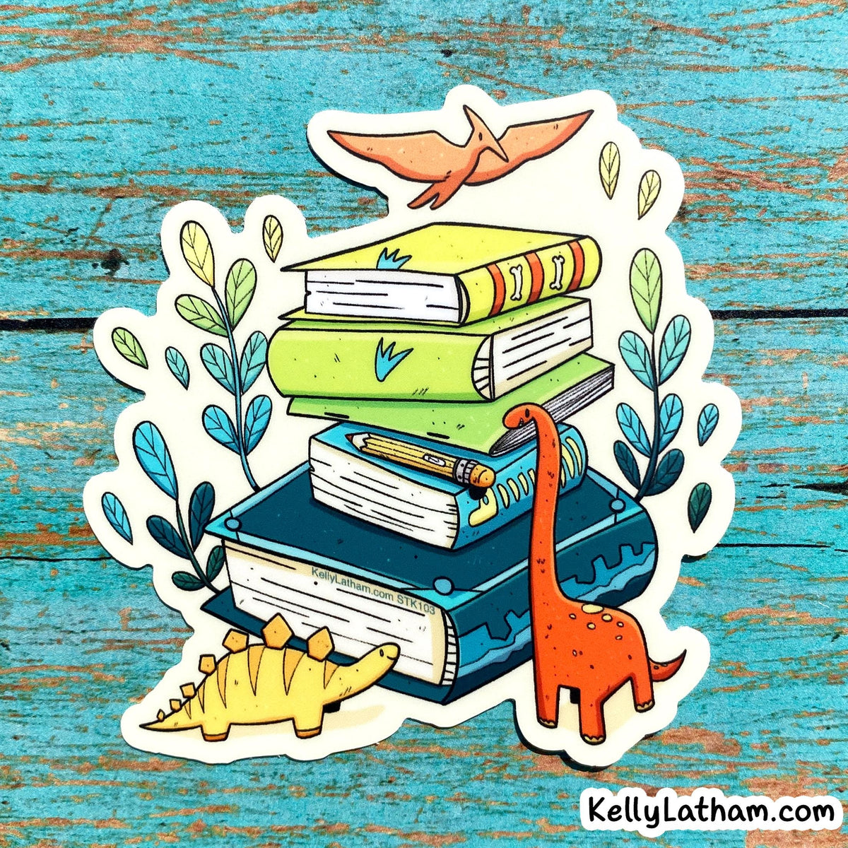 A die-cut sticker featuring a stack of colorful books with cartoon dinosaurs and plants, shown on a distressed blue wooden background. The sticker has a white border and the text 'KellyLatham.