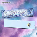 Two rectangular yoga mats shown from different angles on a purple and blue galaxy background. The top mat features an illustrated design of a blue and white dinosaur surrounded by crystals, while the bottom mat is plain white with a small circular cartoon logo in the lower right corner.