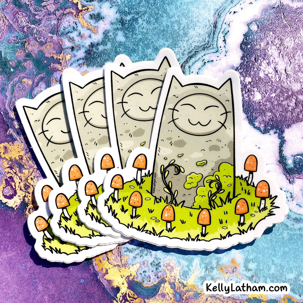 A set of illustrated die-cut stickers showing a smiling cat face on a beige rectangular background, with small orange mushrooms and green grass on the front sticker, arranged on a colorful abstract marbled surface. The text 'KellyLatham.