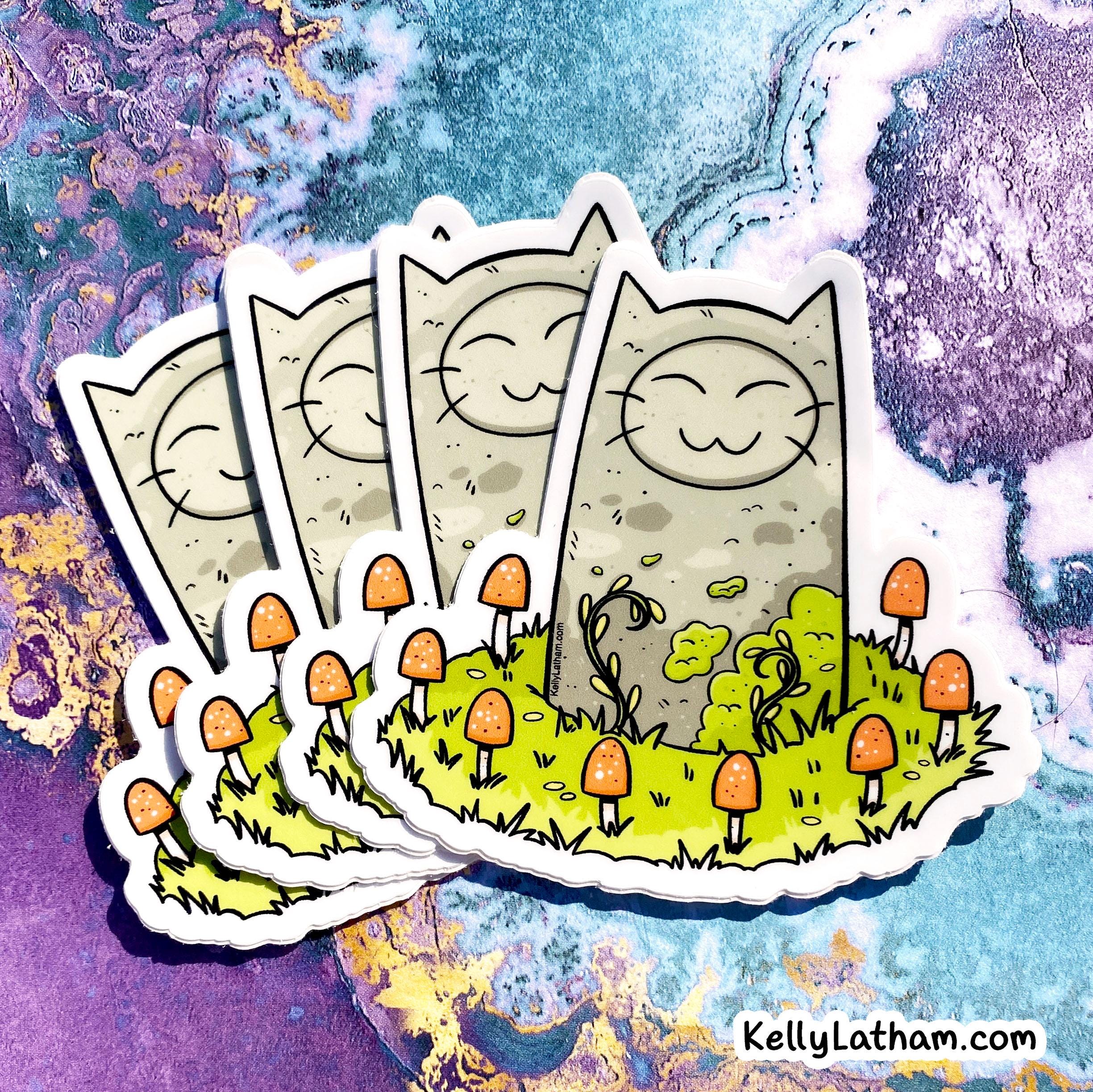 A set of illustrated die-cut stickers showing a smiling cat face on a beige rectangular background, with small orange mushrooms and green grass on the front sticker, arranged on a colorful abstract marbled surface. The text 'KellyLatham.