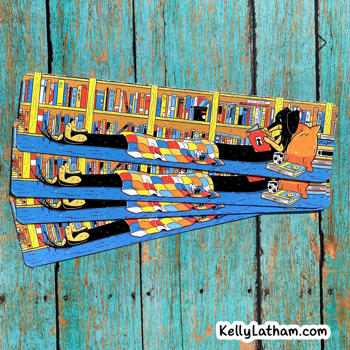 A rectangular printed art piece or book cover featuring a colorful illustrated scene of cartoon animals reading on bookshelves, photographed against a distressed teal wood plank background. A visible watermark reads KellyLatham.