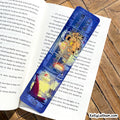 A blue and white illustrated pencil case featuring a cartoon character and the words 'Be Kind, Stay Kind,' placed on top of an open book on a wooden surface.