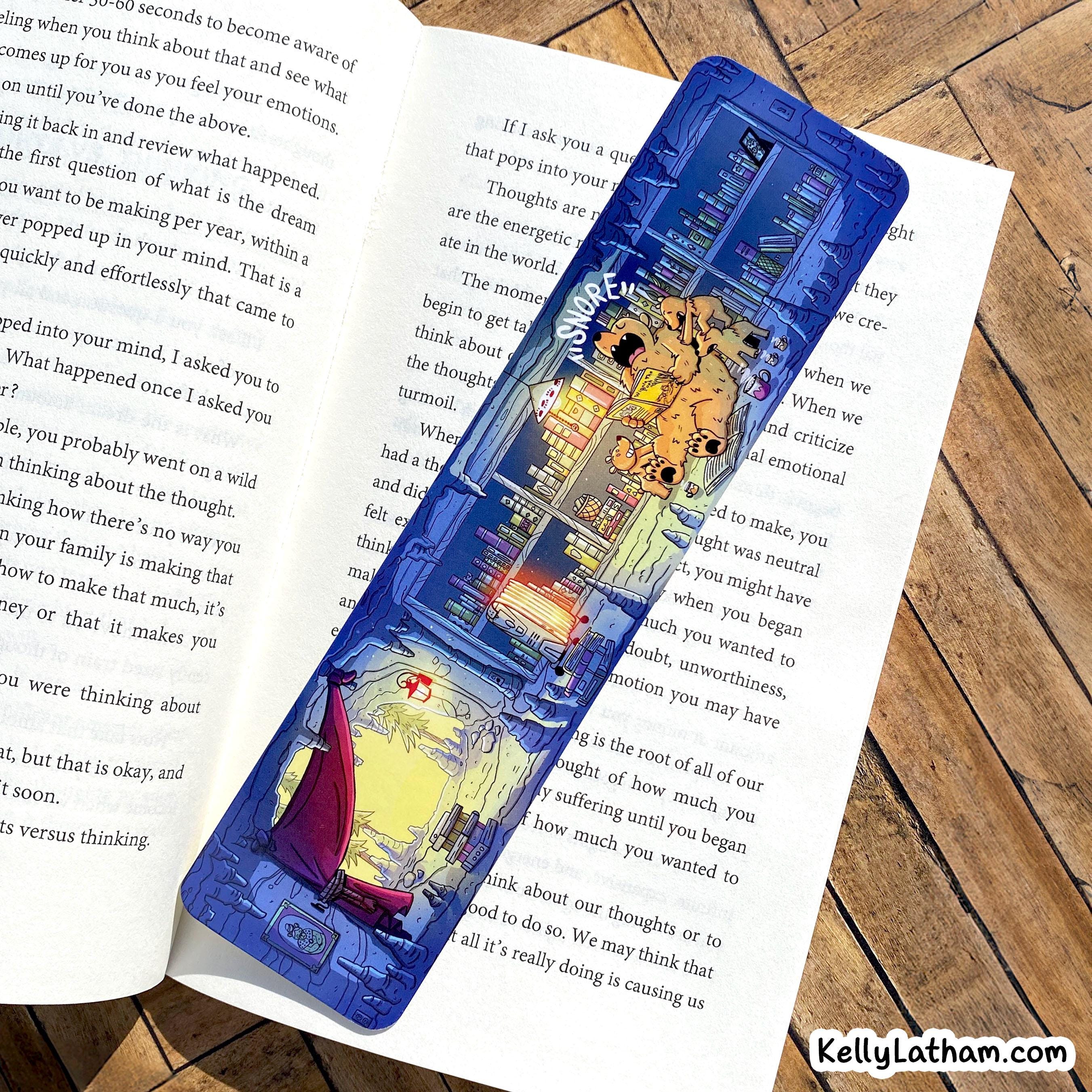 A blue and white illustrated pencil case featuring a cartoon character and the words 'Be Kind, Stay Kind,' placed on top of an open book on a wooden surface.