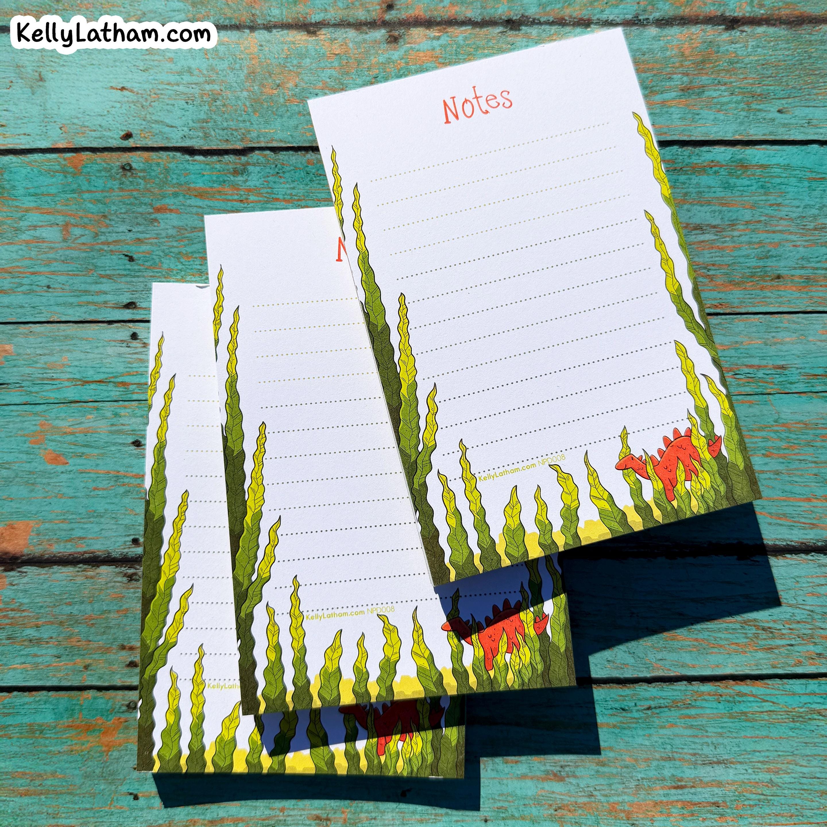 Three lined notes papers with a green seaweed and red dinosaur illustration, arranged on a rustic teal wooden background. The top sheet has 'Notes' printed at the top.