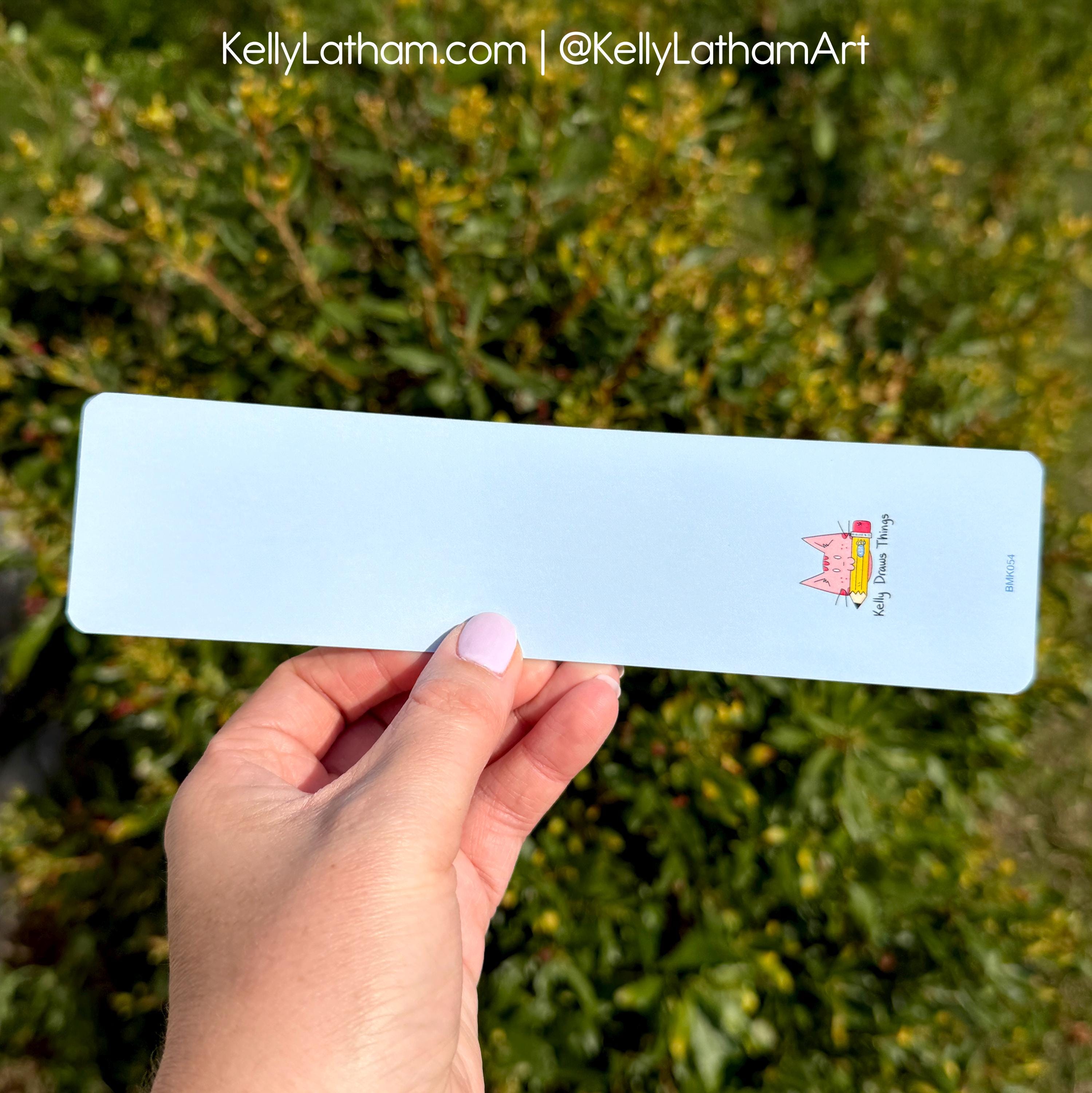 Light blue bookmark with a cartoon character held by a hand against a green leafy background