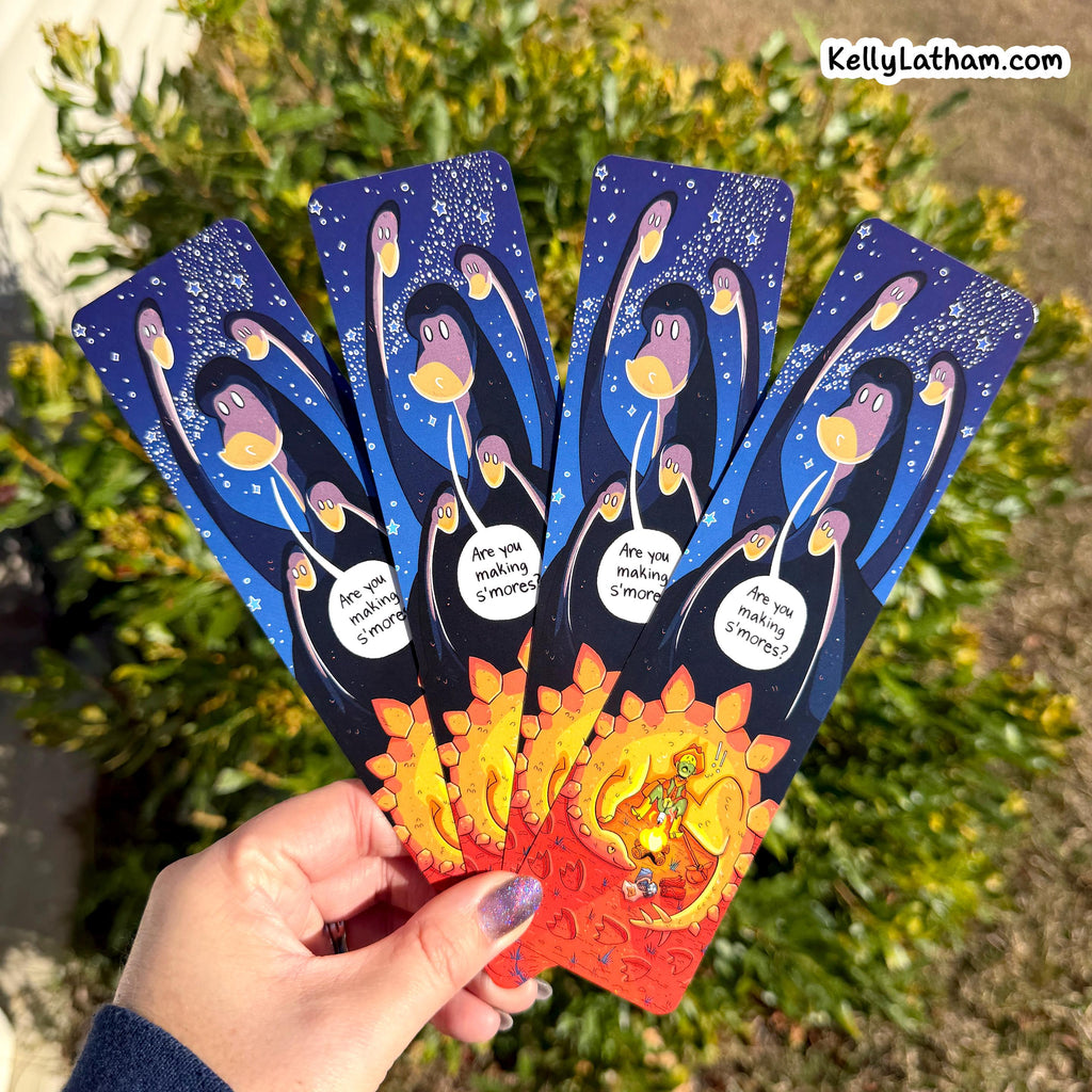 A hand holds four illustrated bookmarks outdoors in front of green bushes. The bookmarks are dark blue with cartoon penguins, white speech bubbles, and a red-to-yellow gradient at the bottom.
