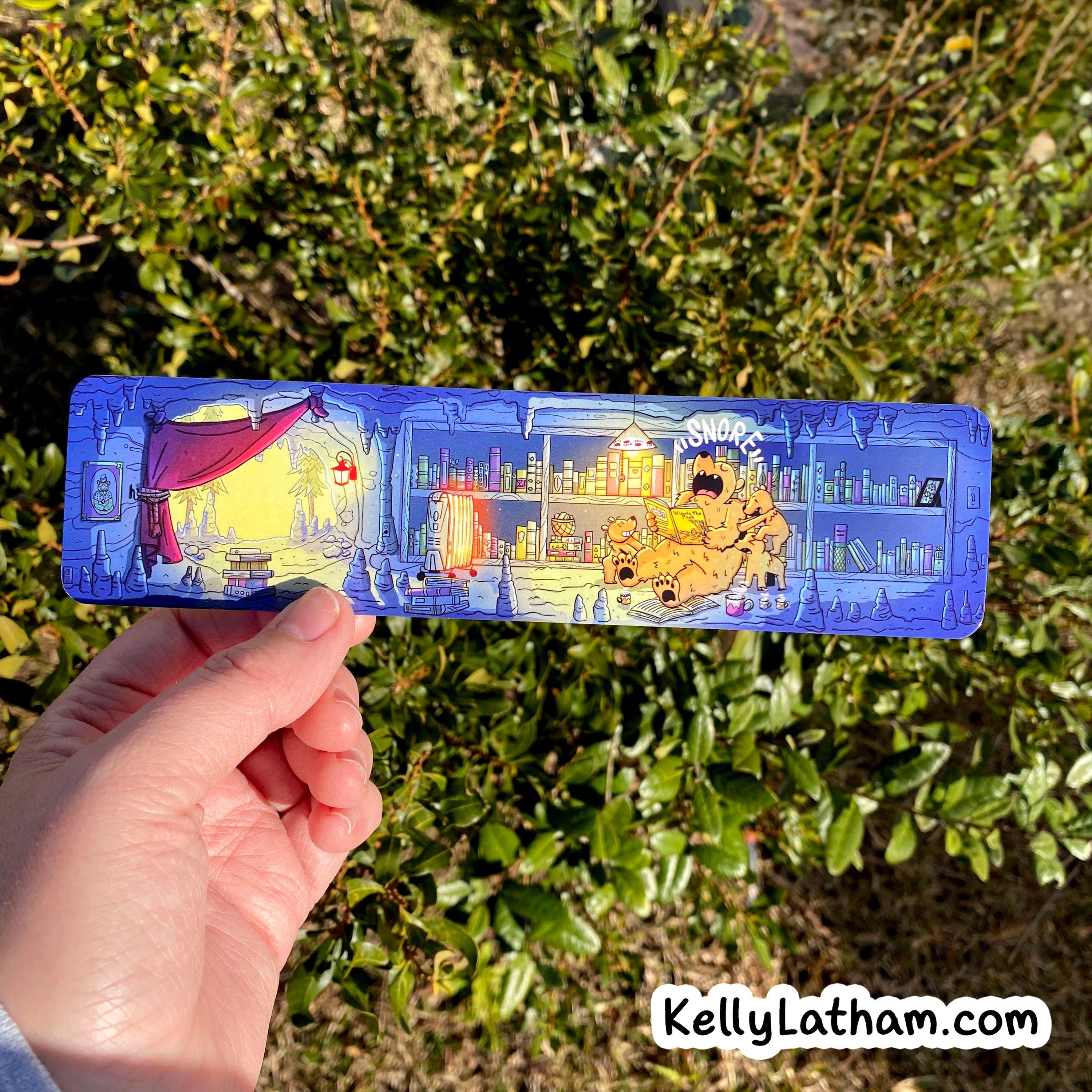 A hand holds a long, narrow illustrated pencil case outdoors in front of green foliage. The pencil case is predominantly blue with a detailed cartoon illustration of a laboratory scene and the word 'AOMRO' at the top.