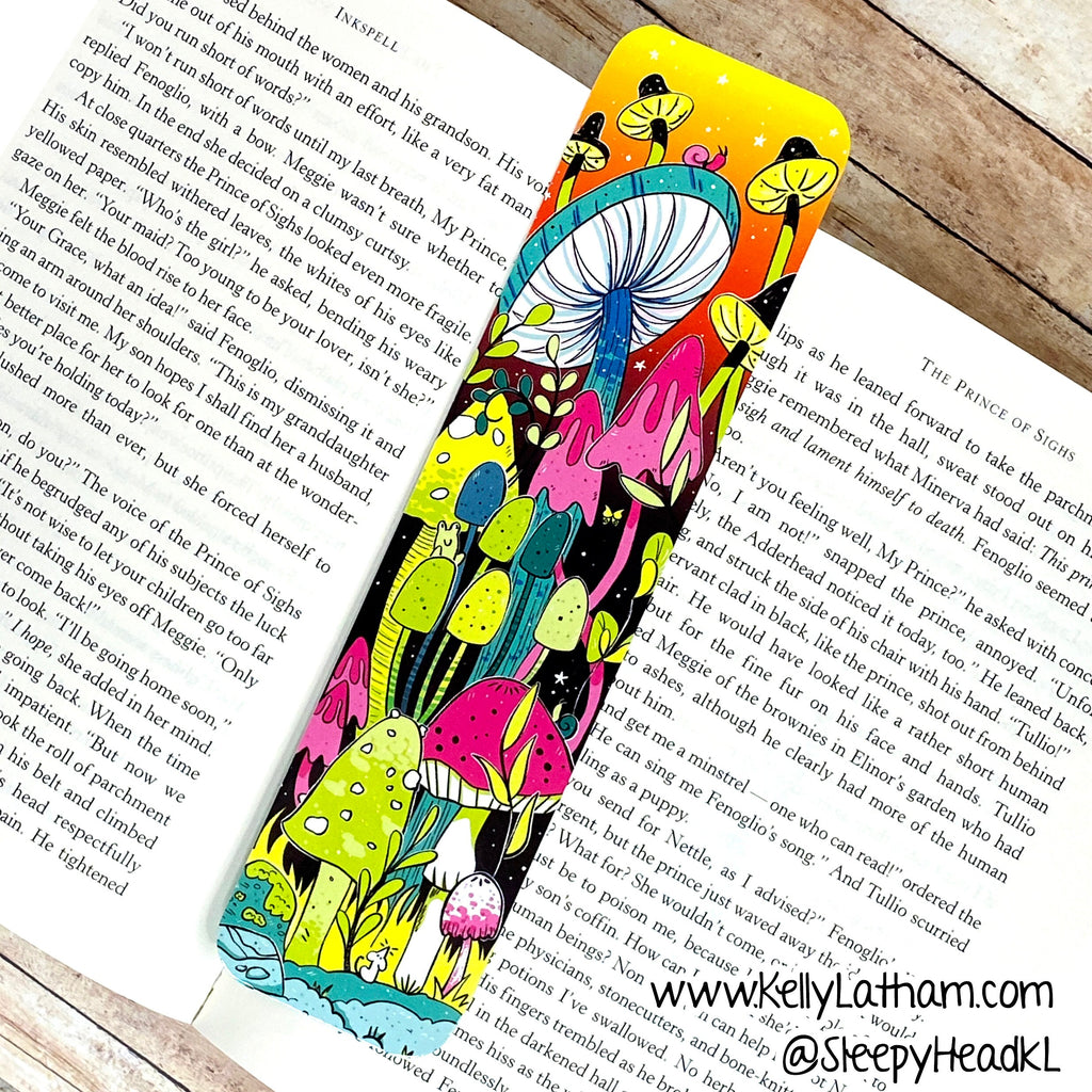 A colorful illustrated bookmark with whimsical fantasy and mushroom artwork rests on open book pages, with a wooden surface visible around it.