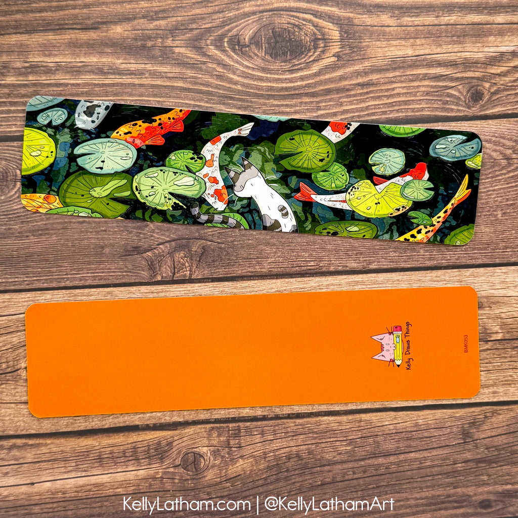 bookmark with fish and lily pad design on a wooden surface, featuring the artist's name.