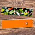 bookmark with fish and lily pad design on a wooden surface, featuring the artist's name.